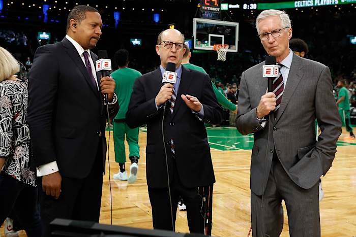 Three ESPN broadcasters stand on the court holding microphones
